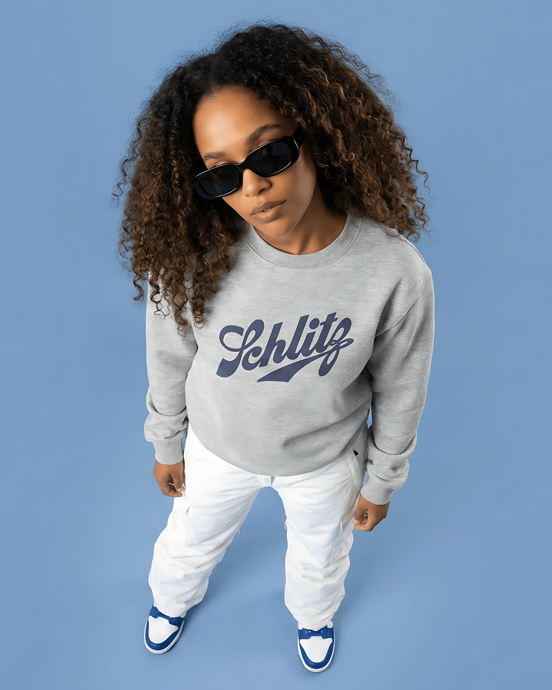 Person wearing SCHLITZ HEAVY SWEATER in gray with sunglasses against a blue background.