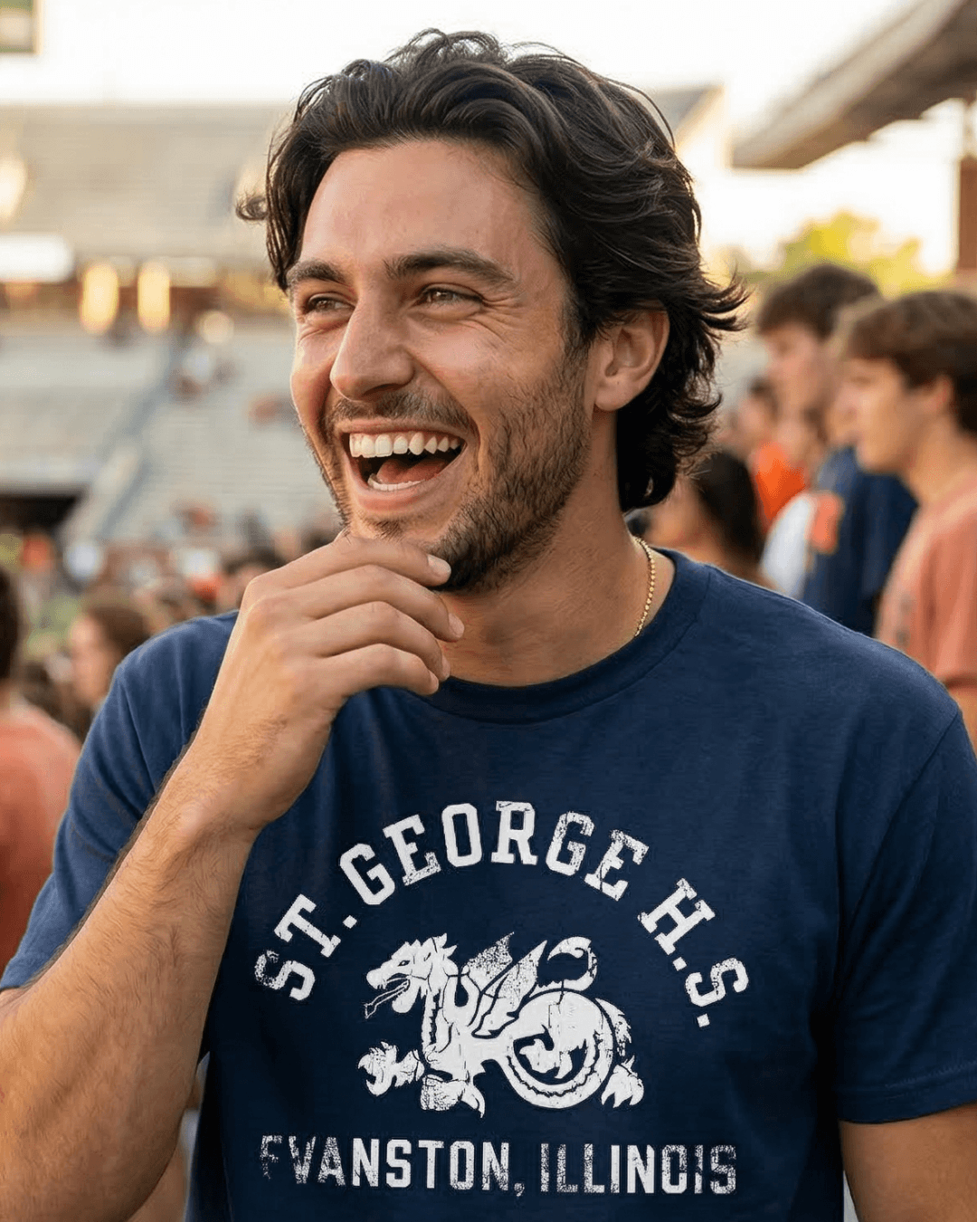 Young man smiling in a crowd wearing a ST. GEORGE HIGH SCHOOL T-SHIRT, showcasing a raw streetwear aesthetic.