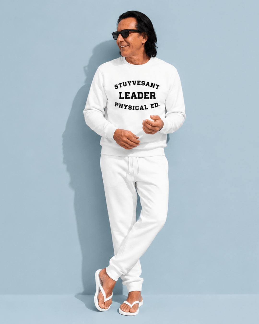 Man wearing a Stuyvesant Leader Heavy Sweater with PHYSICAL ED. lettering, stylishly posed against a light blue background.