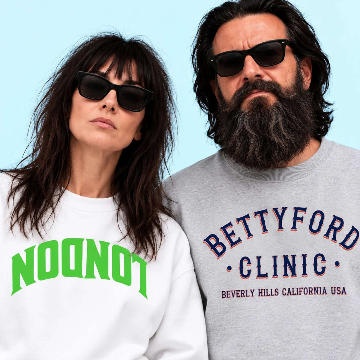 Fashionable couple wearing trendy sweatshirts with 'LONDON' and 'BETTYFORD CLINIC' text, posing against a light blue background.