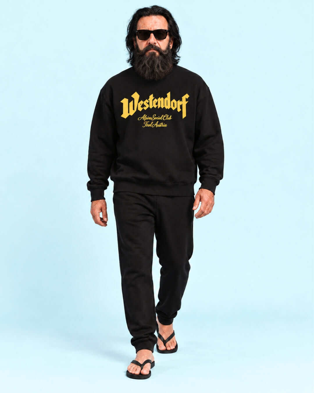 Walter wearing the Black Westendorf Alpine Social Club Heavy Sweater with yellow print and black joggers.